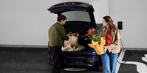 Paar lädt Einkaufstaschen und Pflanzen in Elektroauto-Kofferraum.