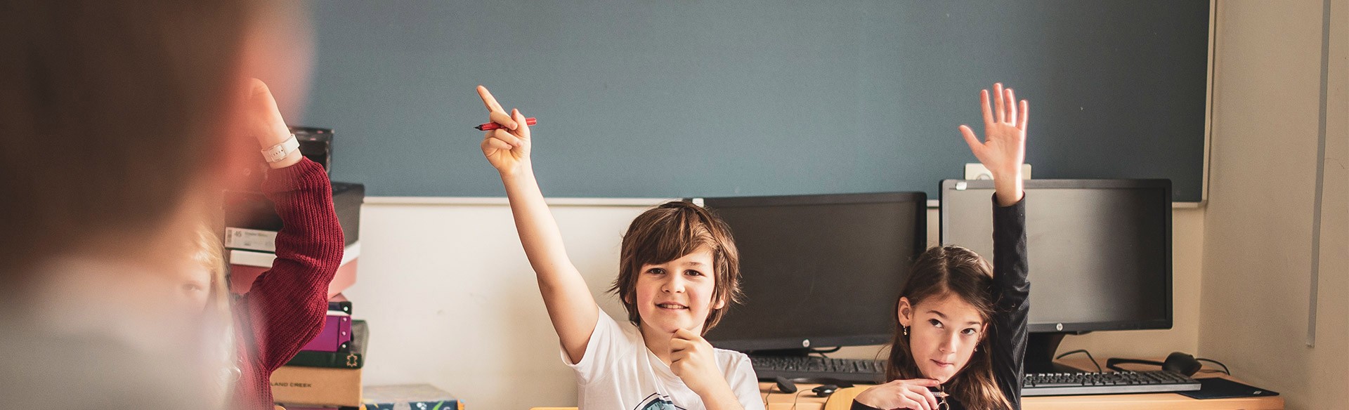 Zwei Kinder im Klassenzimmer melden sich.
