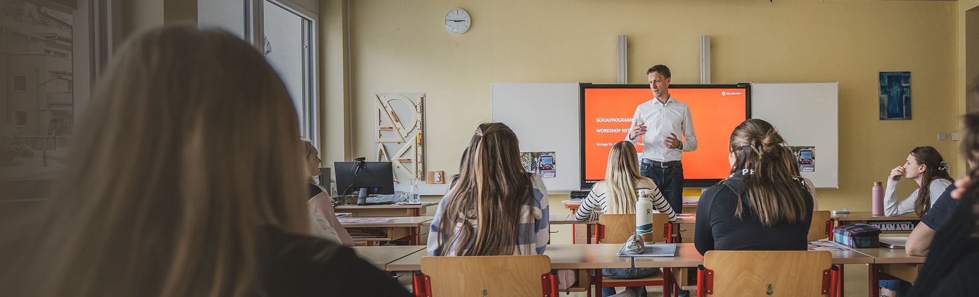 Lehrer präsentiert Schulprogramm im Klassenzimmer.