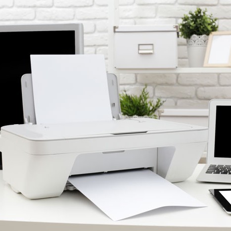 Weißer Drucker mit Papierausgabe, neben Laptop und Büroaccessoires.