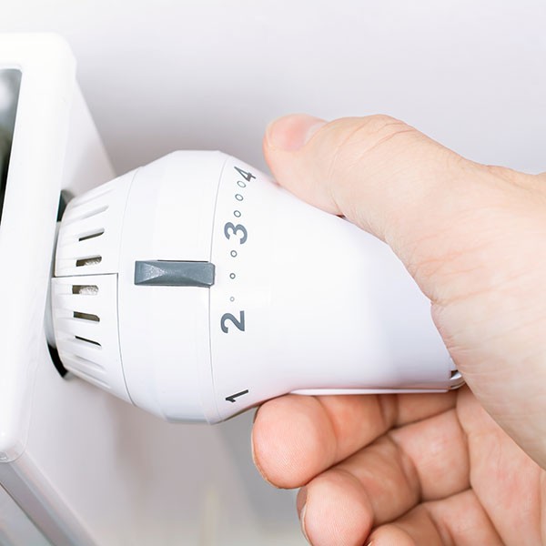 Hand dreht Thermostat an Heizkörper.