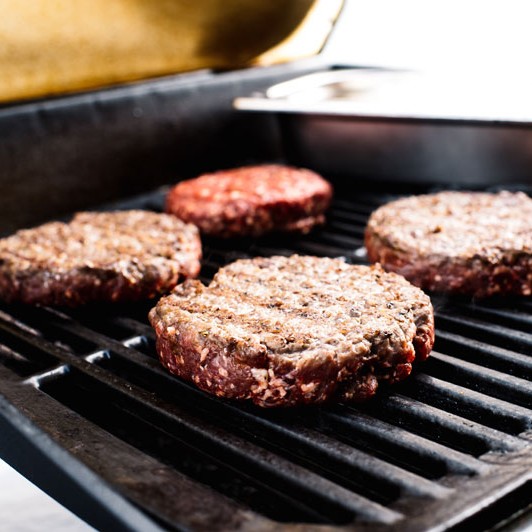 Vier Burgerpattys auf dem Grillrost.