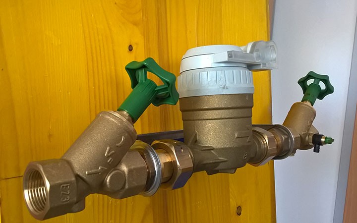 Wasserzähler mit Absperrventilen an Holzwand montiert.