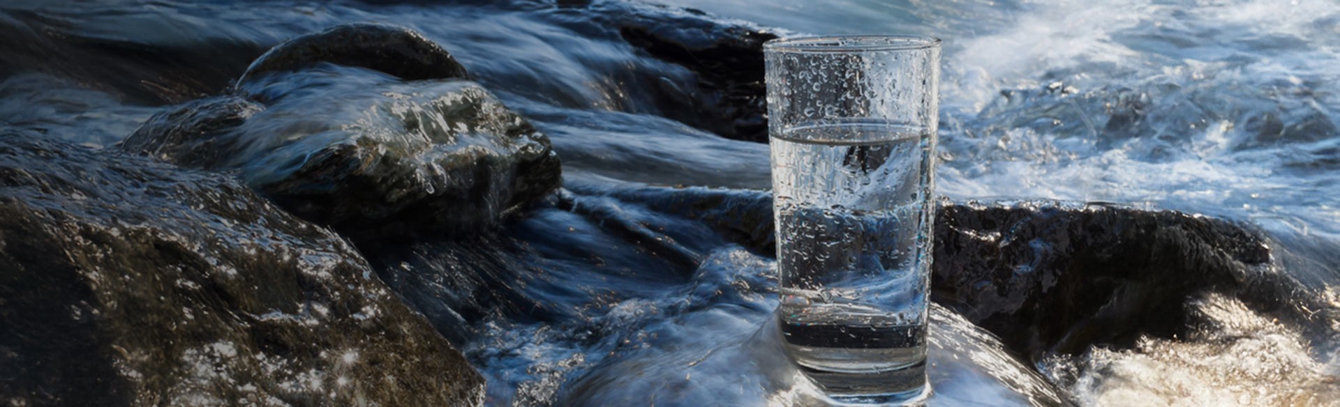 Glas Wasser auf Felsen neben fließendem Bach.