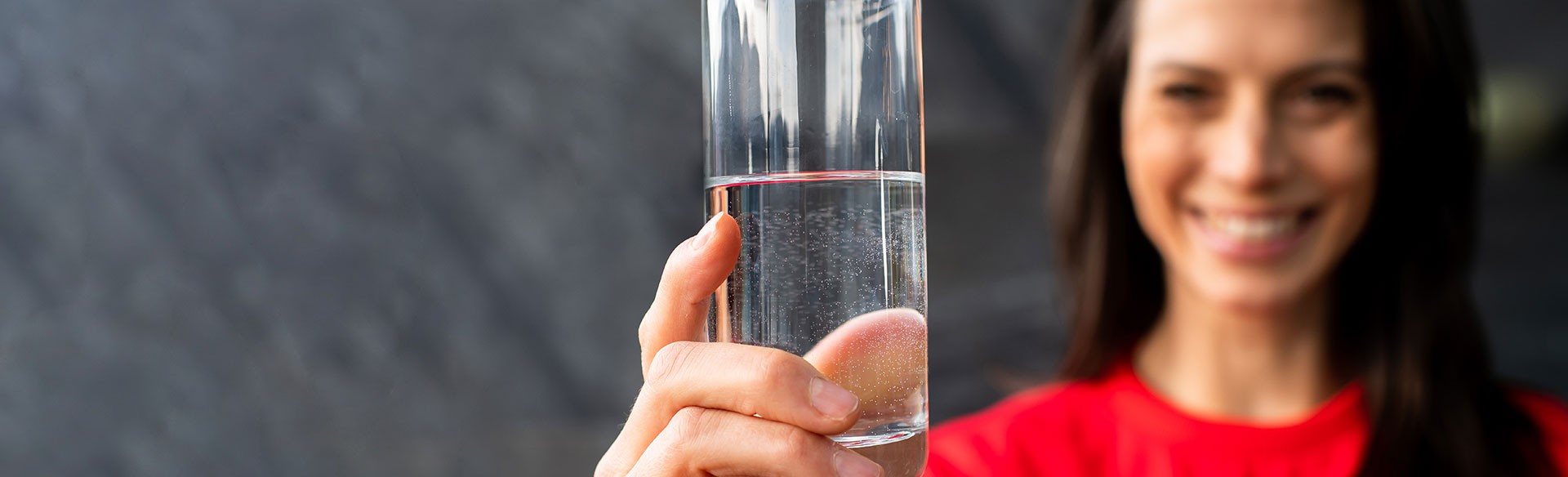 Glas mit Wasser in der Hand einer lächelnden Frau.