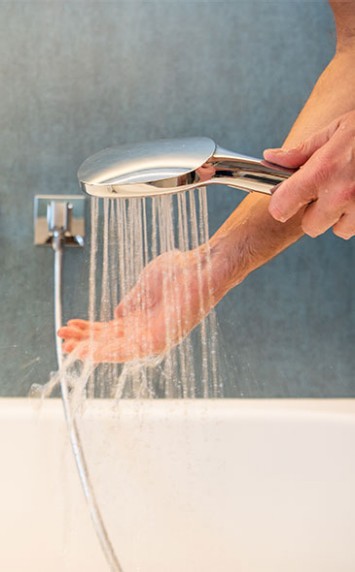 Hand unter Duschbrause mit Wasserstrahl.